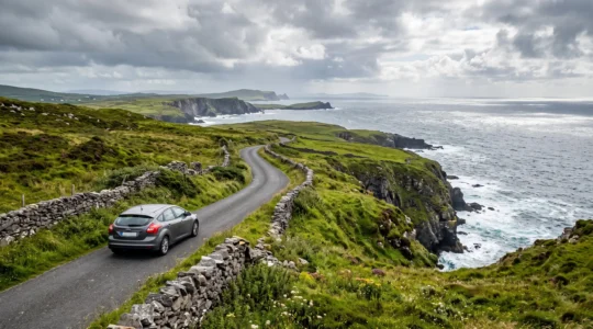 Une voiture circule sur une route côtière sinueuse longeant des falaises verdoyantes sur la côte ouest de l'Irlande.